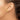 Gold earring worn on a person's ear with a neutral background